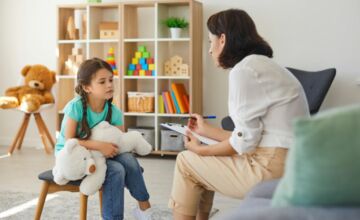 dziewczynka z pluszakiem na kolanach słucha kobiety w tle zabawki