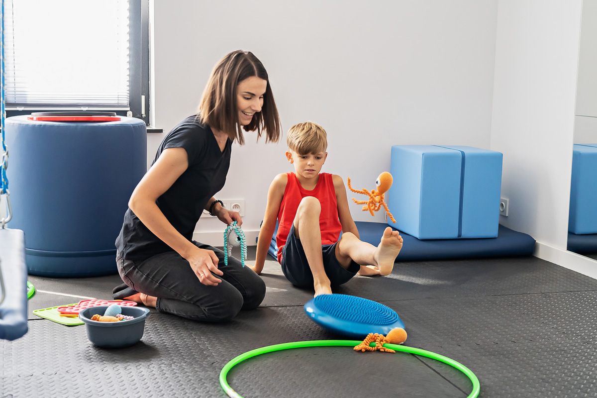 kobieta i chłopiec siedza na podłodze, chłopiec wykonuje ćwiczenia nogami