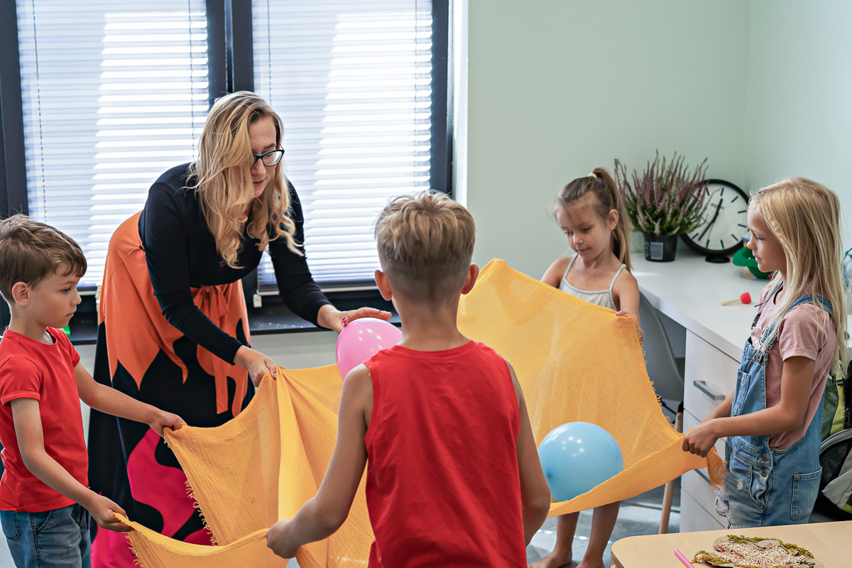 kobieta i czwórka dzieci trzymają koc na którym są kolorowe balony